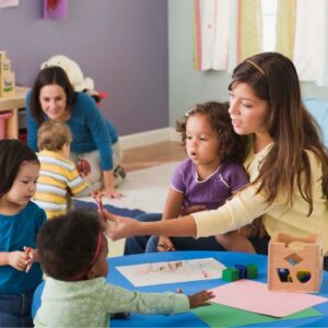 Maestra de centro grupal con niños/as dando una clase en una mesa.