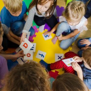 grupo de niños/as en una alfombra jugando con tarjetas del abecedario con una maestra de educacion infantil.