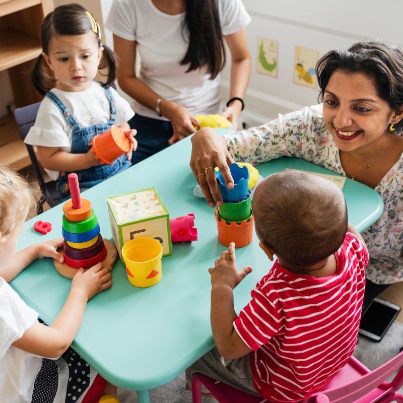 Child care teacher playing at a table with kids and blocks