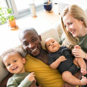 Esposo y esposa en el sofá con sus hijos/as pequeños/as sonriendo a la cámara